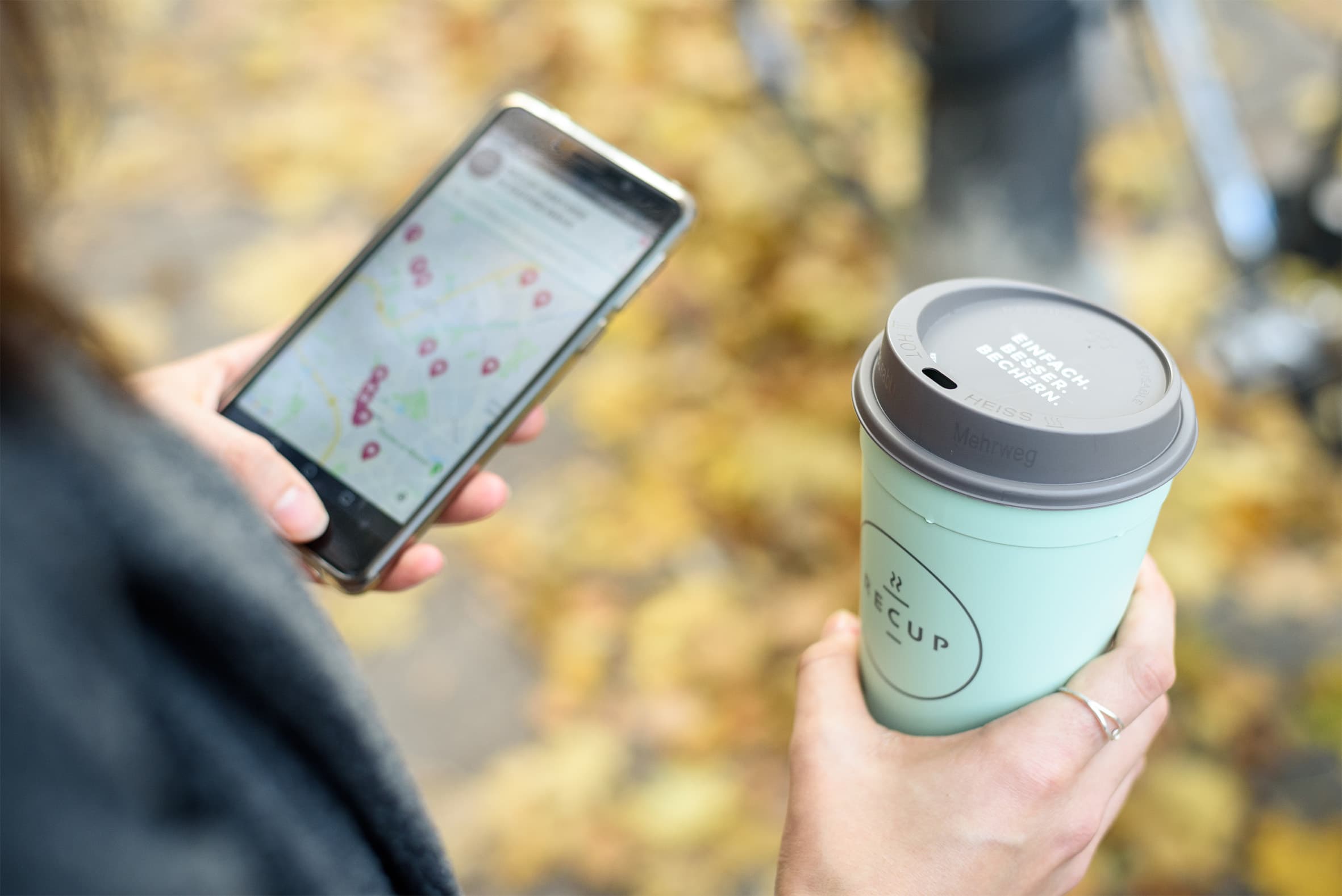 Person mit RECUP-Pfandbecher und Smartphone in der Hand