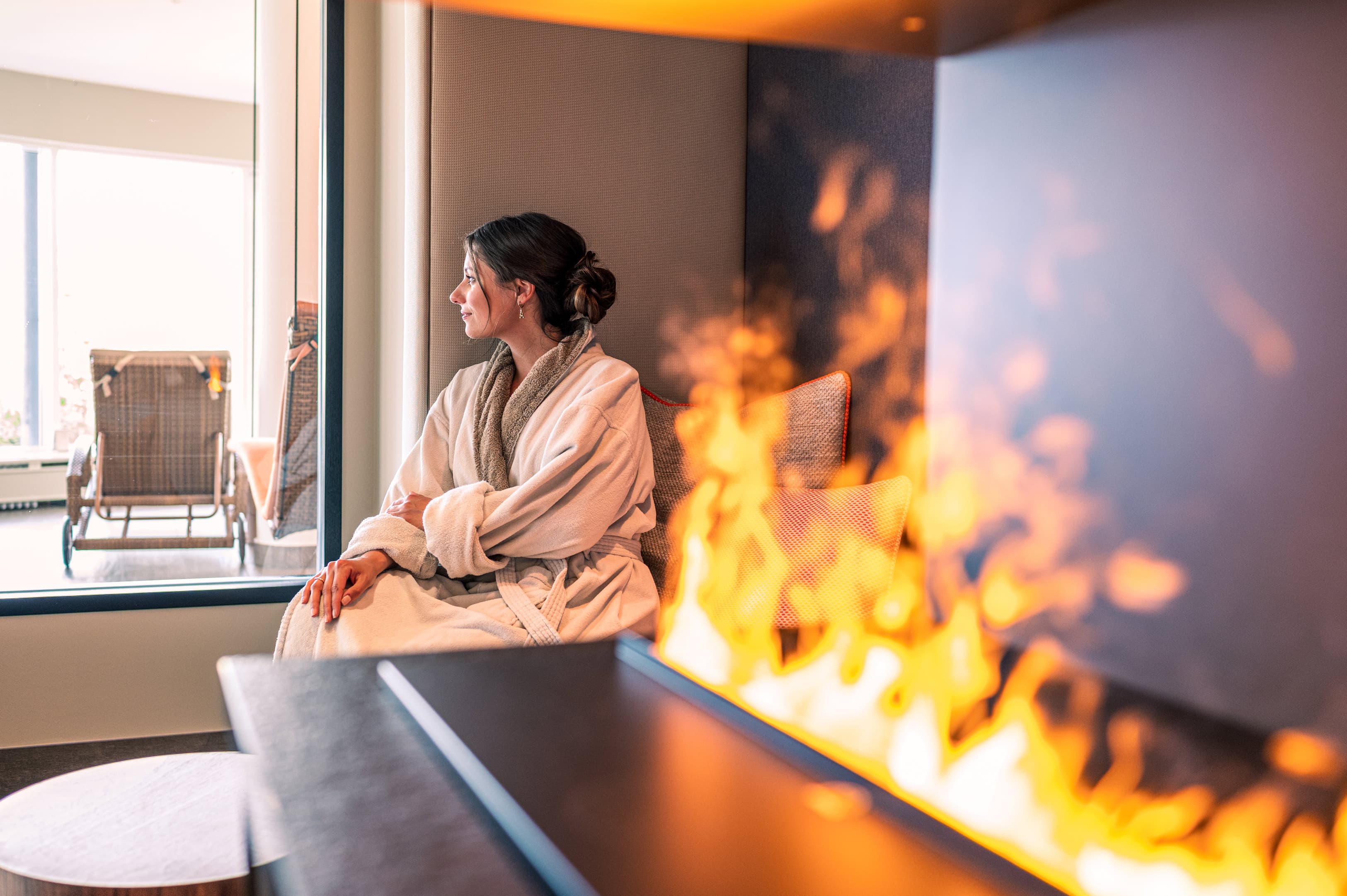Frau sitz am Feuer in einer SPA-Lounge und schaut aus dem Fenster.