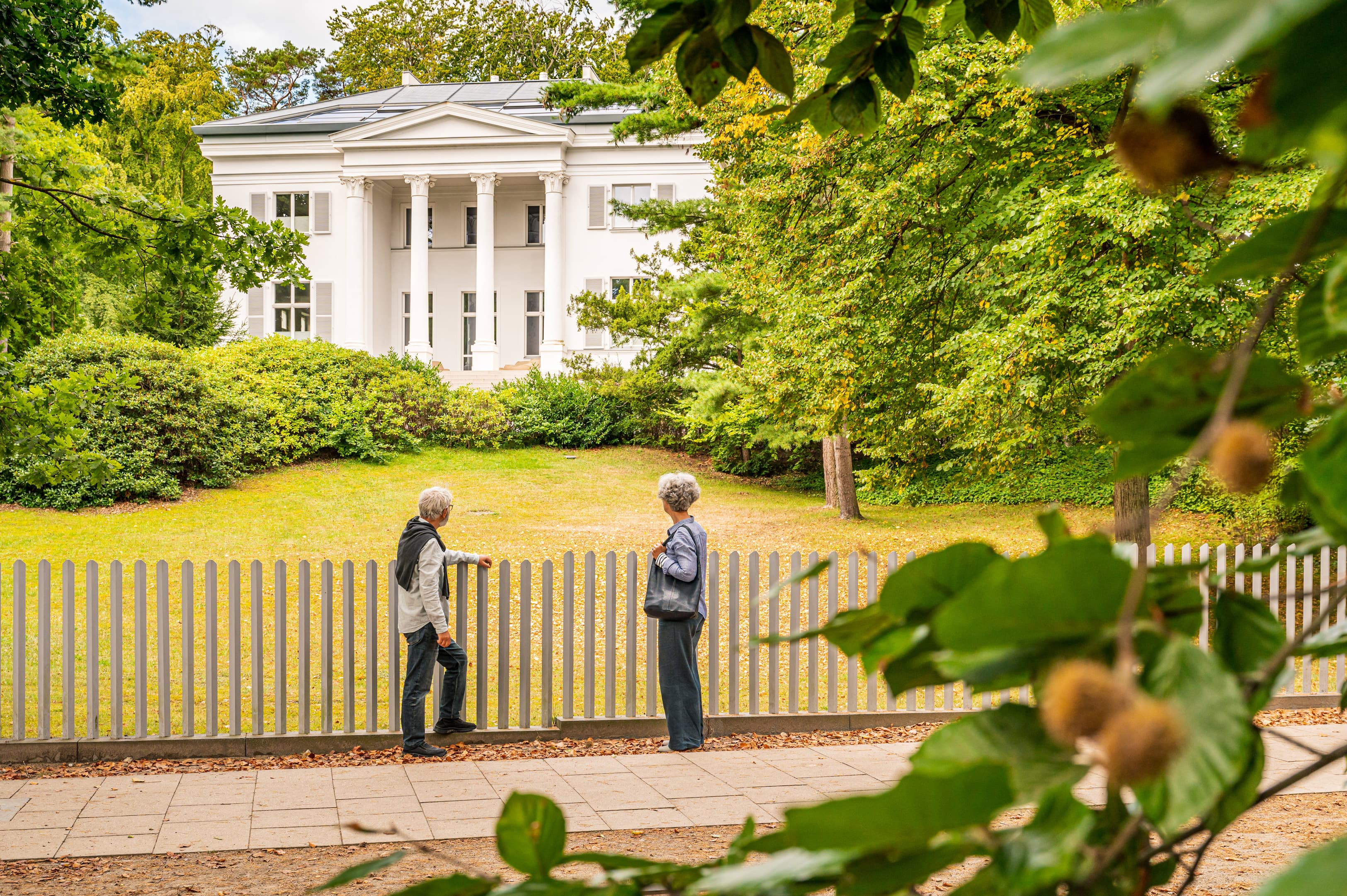 Pärchen steht an einem Zaun und betrachtet eine Bäderarchitektur-Villa.