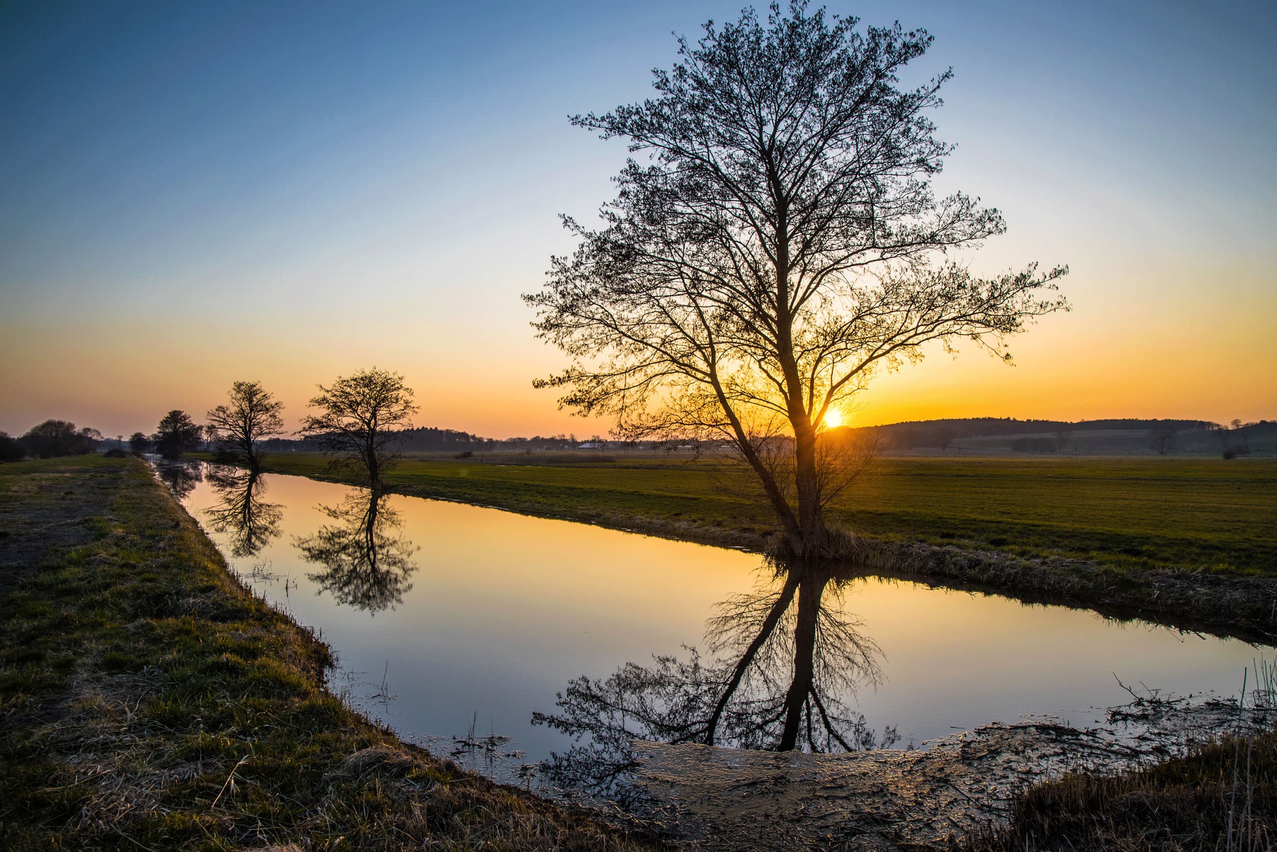 Das Bild zeigt einen Wasserlauf im Thurbruch bei Sonnenuntergang.