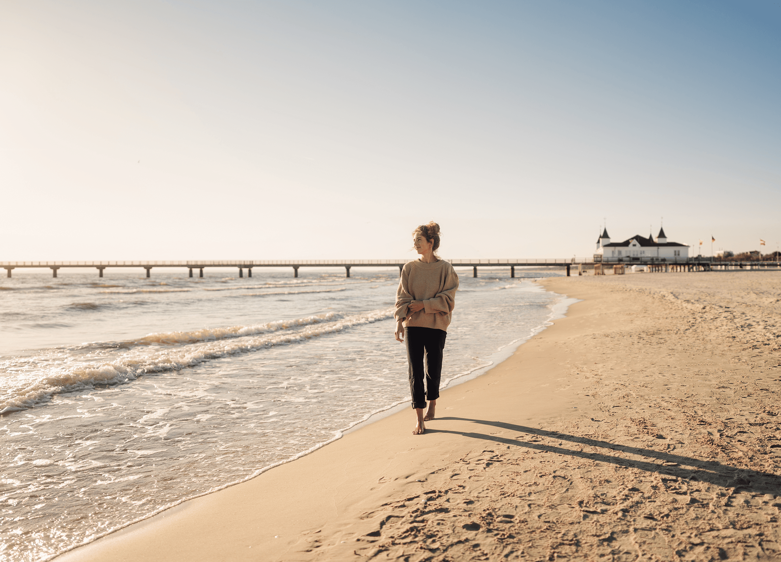 Frau spaziert am Strand von Ahlbeck, im Hintergrund die Seebrücke