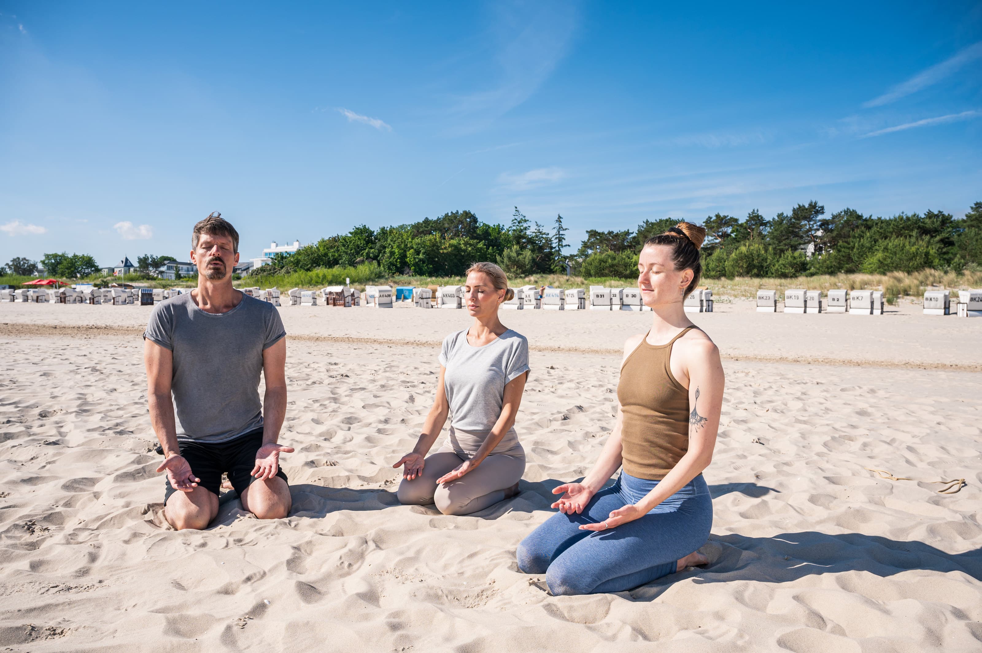 Drei Personen beim Meditieren beim Yoga am Strand.
